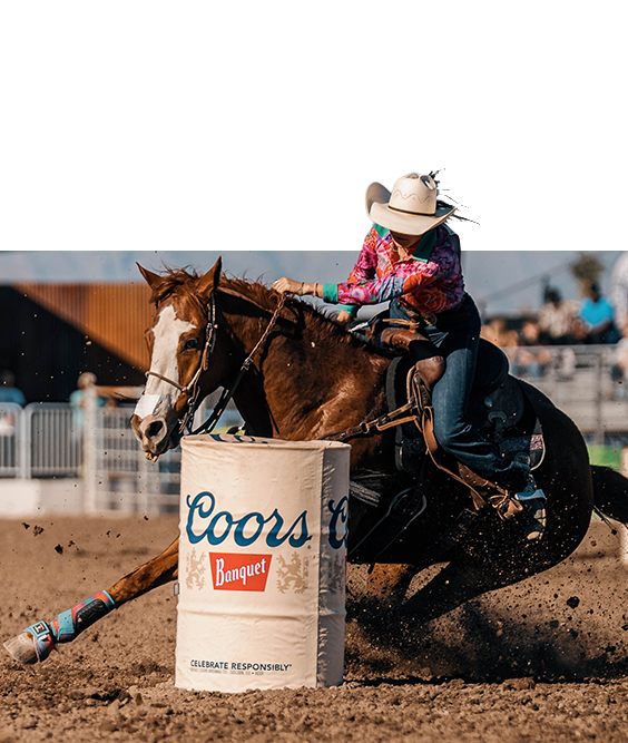 A barrel racer in a pink shirt turns her horse tight around a Coors Banquet barrel.