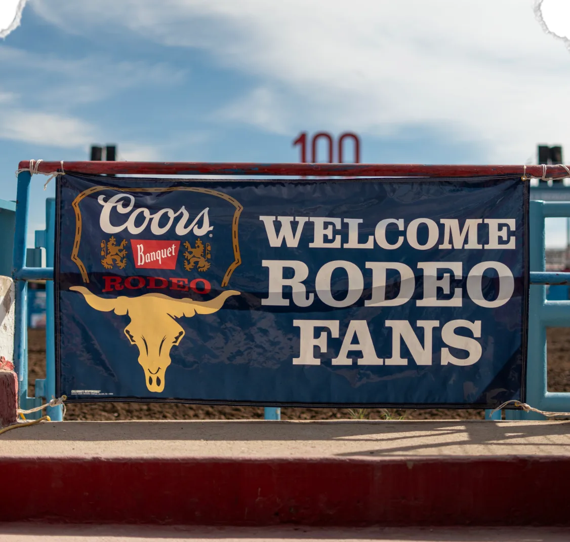A Coors Banquet Rodeo banner reading “Welcome Rodeo Fans” hangs on the arena fence.