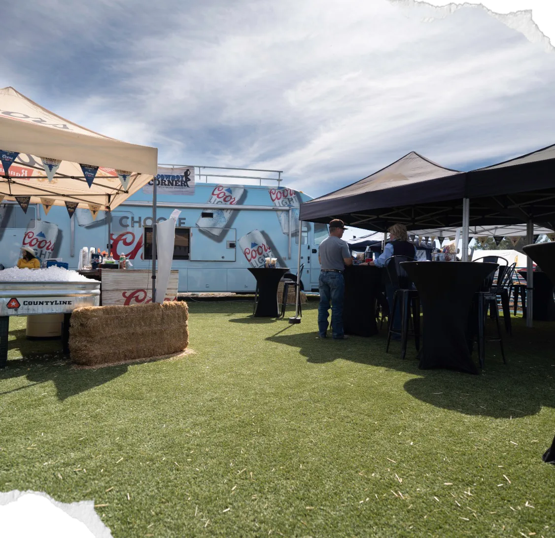 A grass hospitality area with tents and hay bales at Coors Cowboy Corner.