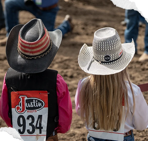 Two young competitors in cowboy hats and back numbers, seen from behind